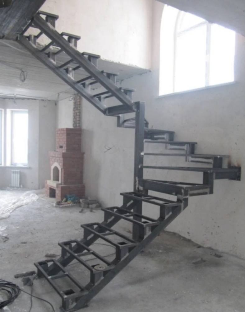 Metalowa konstrukcja schodów spiralnych w trakcie montażu w surowym wnętrzu w Warszawie, widoczny niedokończony kominek z cegły.