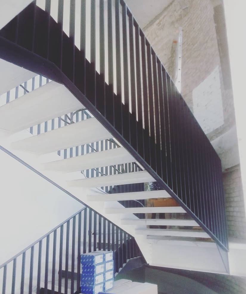 Nowoczesne schody z białymi stopniami i czarną metalową balustradą, widok z dołu, na dole kartony z materiałami budowlanymi.