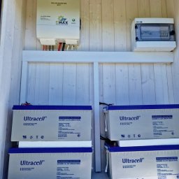 ELMAX SPÓŁKA Z OGRANICZONĄ ODPOWIEDZIALNOŚCIĄ - Wnętrze szafy z zamontowanym inwerterem solarnym Volt Polska, rozdzielnicą elektryczną i czterema akumulatorami Ultracell UCG200-12, całość w drewnianej obudowie.