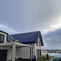 ELMAX SPÓŁKA Z OGRANICZONĄ ODPOWIEDZIALNOŚCIĄ - Montaż paneli słonecznych na dachu nowoczesnego domu z widocznymi pracownikami i samochodem firmy na tle zimowego krajobrazu.