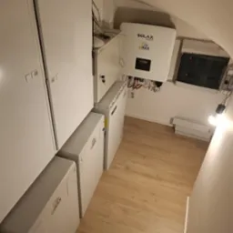 Instalacja magazynu energii Solax Power EMAX z inwerterem i rozdzielnicą elektryczną w pomieszczeniu oświetlonym żarówką