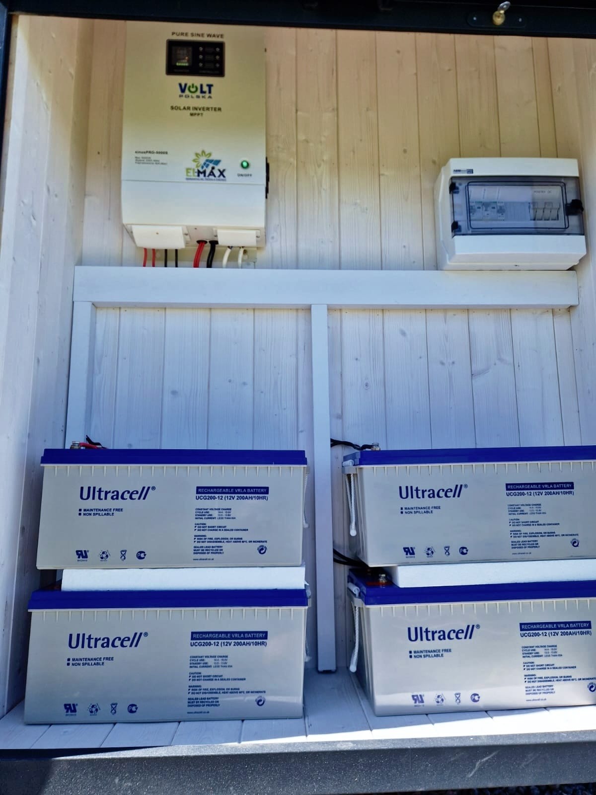 Wnętrze szafy z zamontowanym inwerterem solarnym Volt Polska, rozdzielnicą elektryczną i czterema akumulatorami Ultracell UCG200-12, całość w drewnianej obudowie.