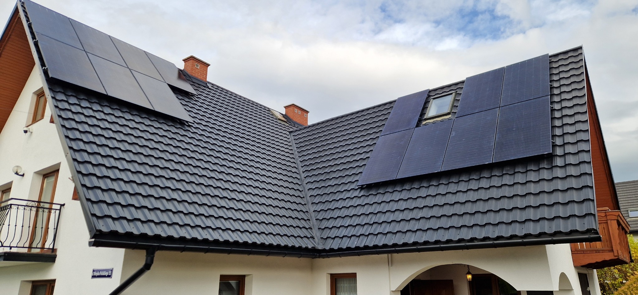Czarny dach z blachodachówki z zamontowanymi panelami słonecznymi na białym domu z balkonem.
