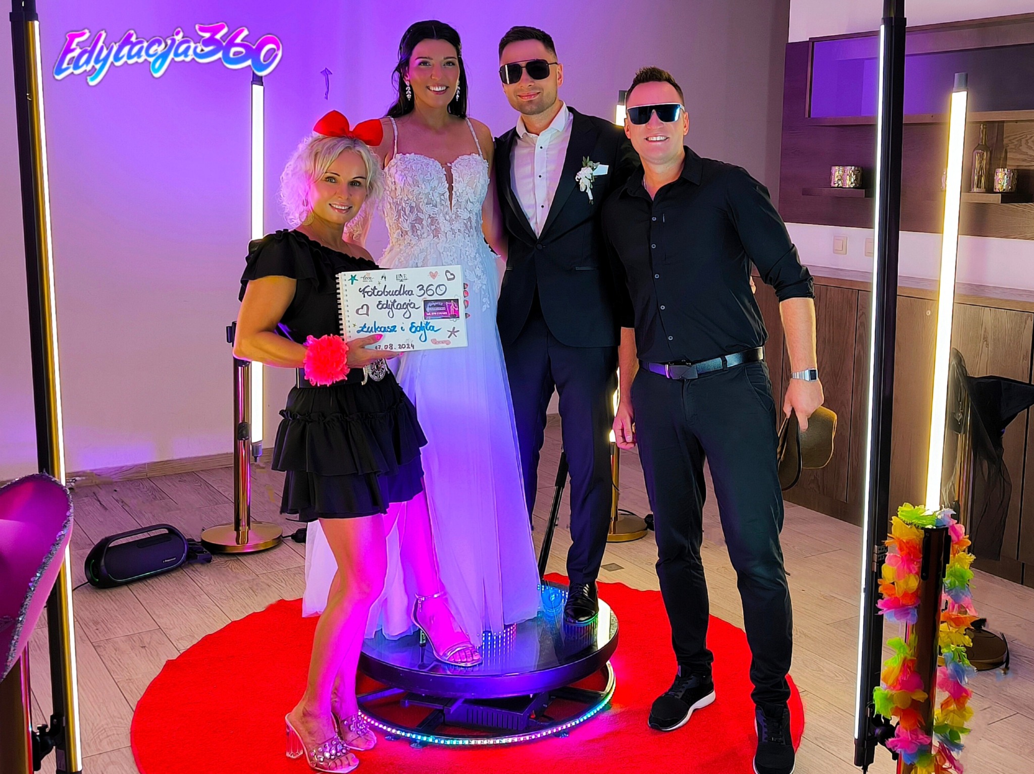 Para młoda i goście pozują na obrotowej platformie ze światełkami, trzymając tabliczkę z napisem 'Fotobudka 360'