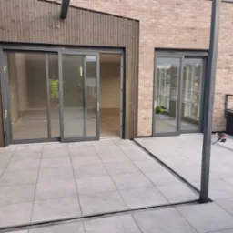 Nowoczesny taras w Tychowie z szarymi płytkami, widoczne przesuwne drzwi balkonowe z szarą ramą i fragment miasta w tle.