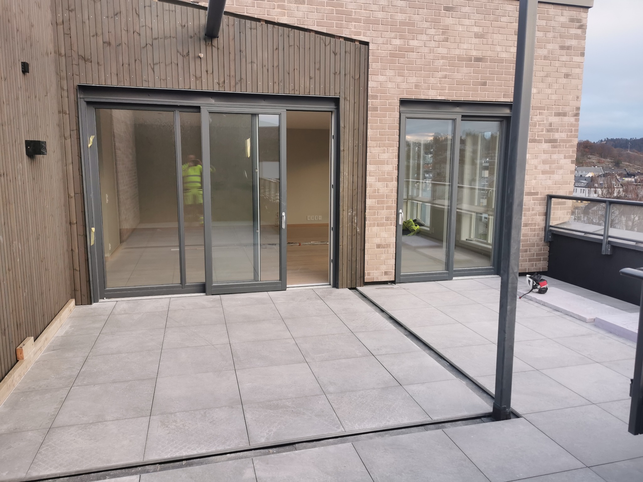 Nowoczesny taras w Tychowie z szarymi płytkami, widoczne przesuwne drzwi balkonowe z szarą ramą i fragment miasta w tle.