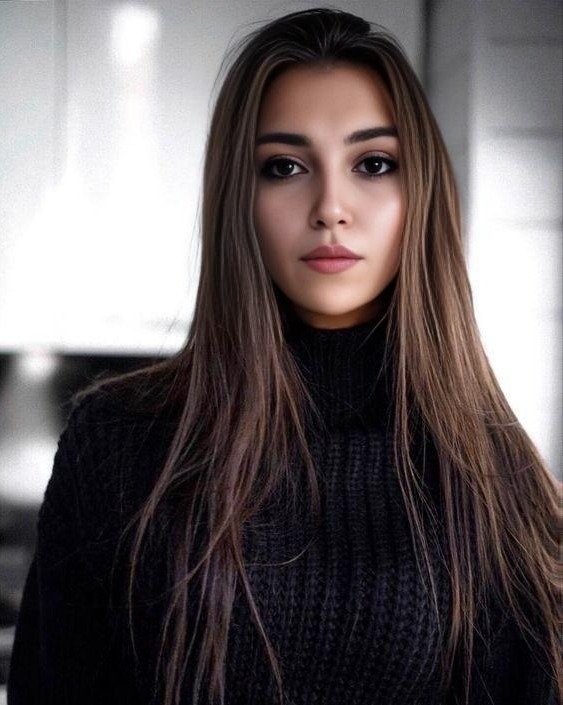 Portret kobiety o długich, prostych, brązowych włosach, ubrana w czarny golf, z delikatnym makijażem i poważnym wyrazem twarzy, na rozmytym, jasnym tle.