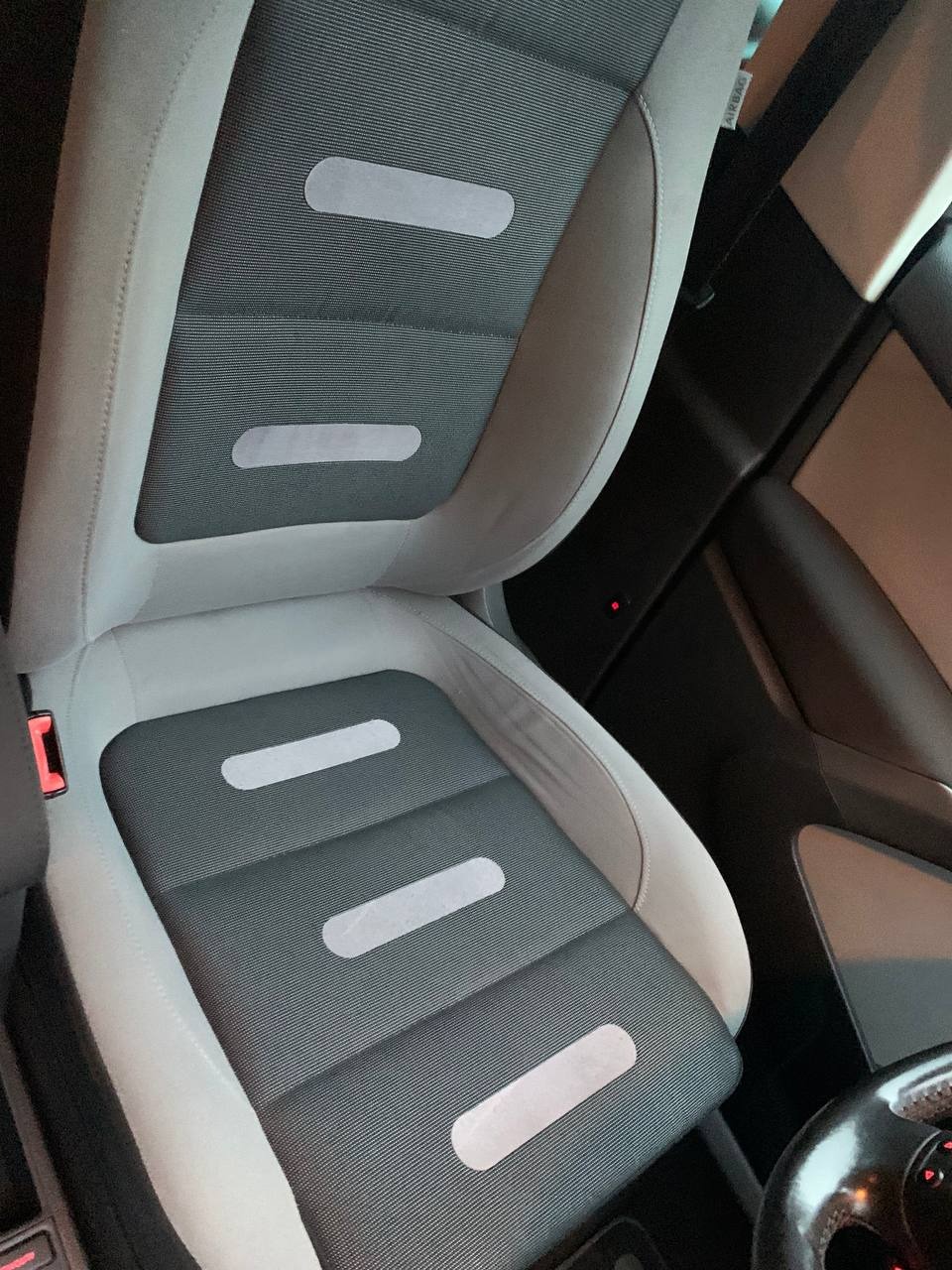 Czyste, szare siedzenie samochodowe z tkaniny z jasnymi, podłużnymi przeszyciami, widoczne elementy wnętrza pojazdu.