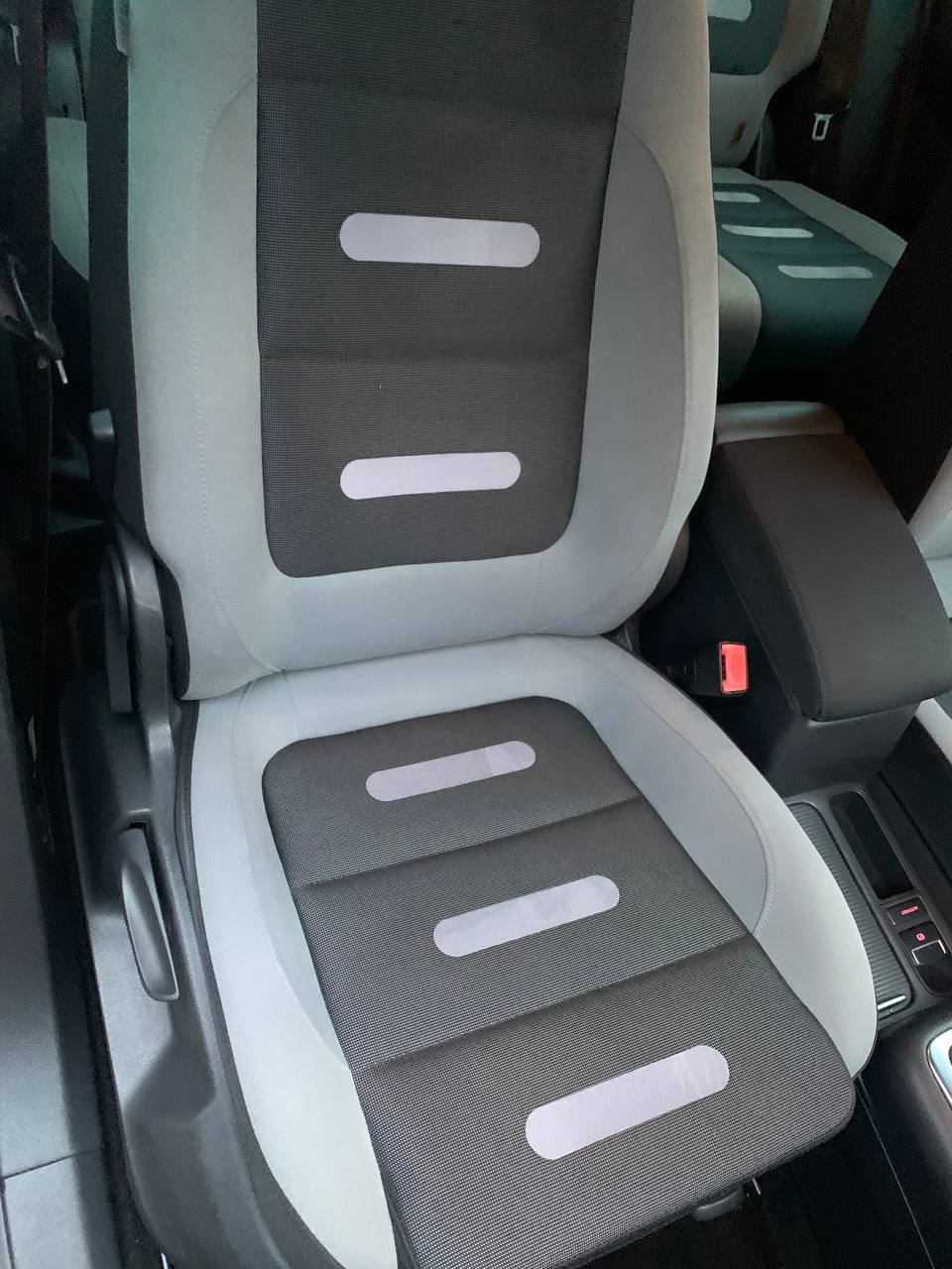 Szare i czarne siedzenie samochodowe z podłużnymi, jasnymi wstawkami, widoczne z bliska, z elementami deski rozdzielczej w tle.