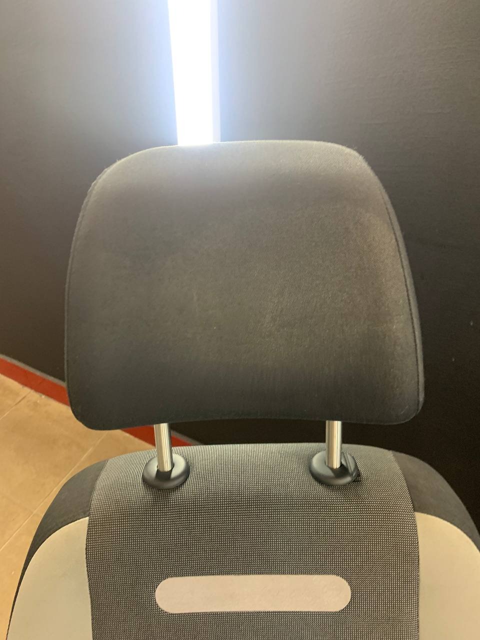 Tapicerowane krzesło z czarnym zagłówkiem i szarą tkaniną w drobną kratkę, widok z tyłu, oświetlone jasnym światłem z góry.