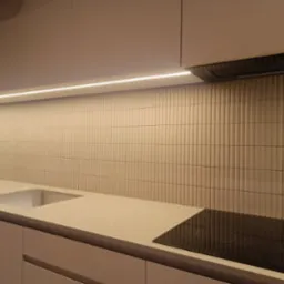 Beżowa kuchnia z płytkami ułożonymi pionowo na ścianie, podświetlenie LED pod szafkami, płyta indukcyjna i wbudowany zlew.