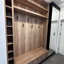 Antima - Wnękowa szafa z siedziskiem i otwartymi półkami, wykończona drewnopodobną okleiną w odcieniach beżu i brązu, z czarnymi haczykami na ubrania i lustrem na drzwiach przesuwnych.