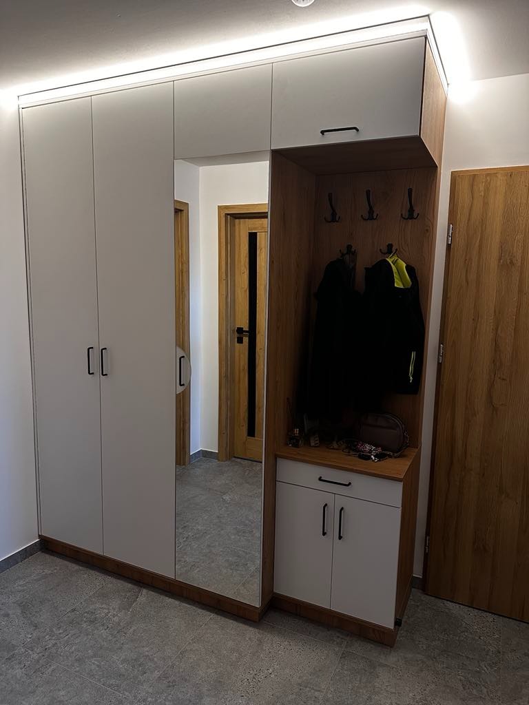 Nowoczesna szafa wnękowa z lustrem i oświetleniem LED, z częścią otwartą na ubrania i akcesoria, w przedpokoju z szarą podłogą.