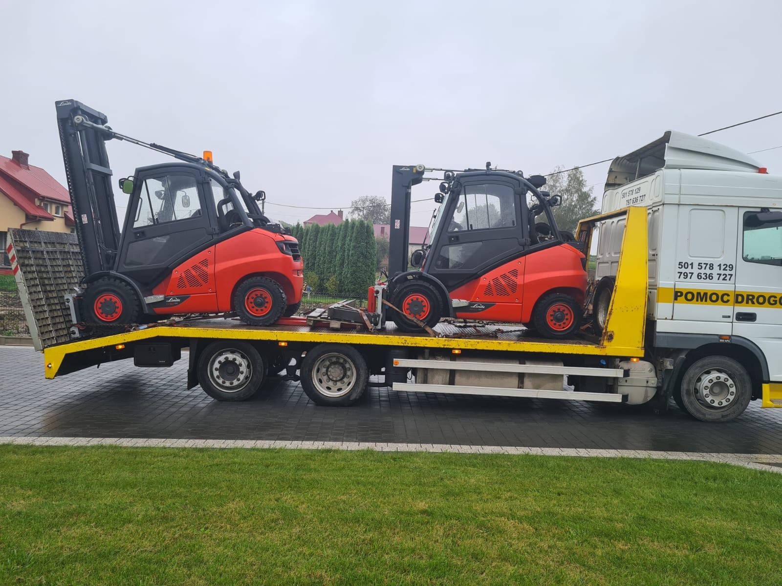 Dwa wózki widłowe Linde w kolorze pomarańczowo-czarnym, przewożone na żółtej lawecie pomocy drogowej. Widoczne numery telefonu na kabinie lawety.