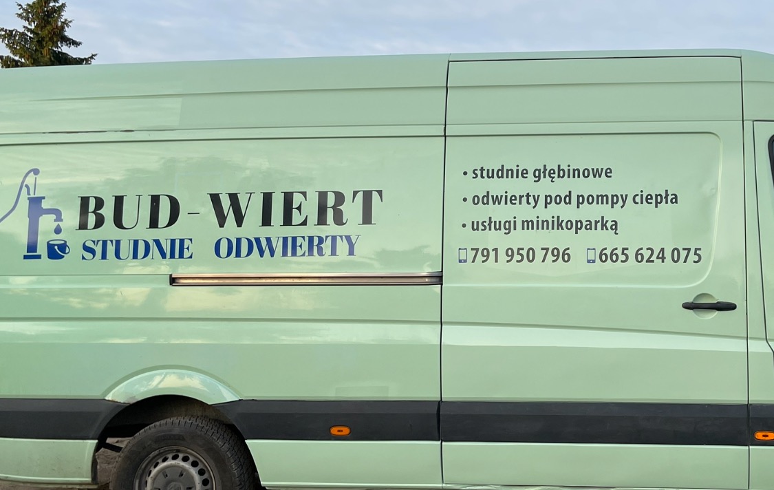 Bok jasnozielonego samochodu dostawczego z niebiesko-czarnym nadrukiem reklamowym firmy 'Bud-Wiert Studnie Odwierty', oferującej usługi wiercenia studni głębinowych i odwiertów pod pompy ciepła...