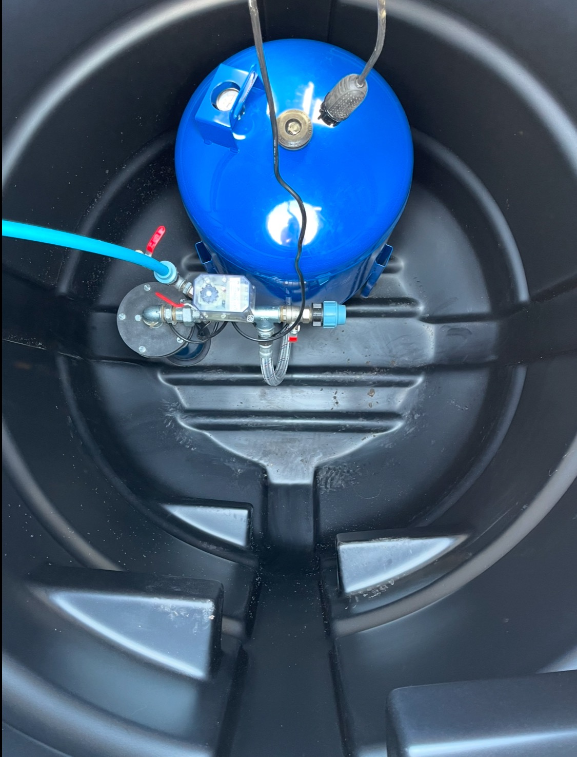 Niebieski zbiornik hydroforowy z osprzętem w czarnym, plastikowym zbiorniku, widok z góry.