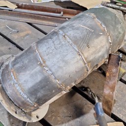 Karspaw - Metalowy cylinder z widocznymi spawami na stole warsztatowym, obok leży palnik spawalniczy, a w tle widać elementy metalowe i zieloną szafkę.