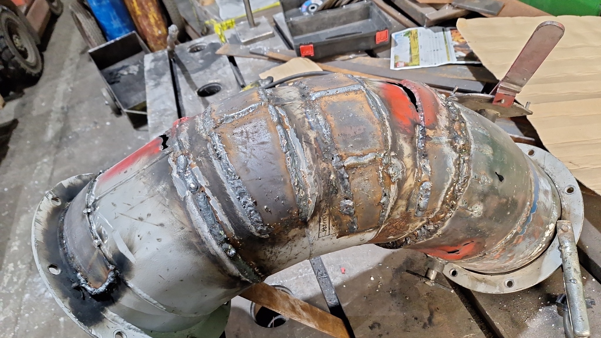 Fragment rury przemysłowej z widocznymi spawami, mocowana za pomocą kołnierzy, leżąca na stole warsztatowym w trakcie obróbki.