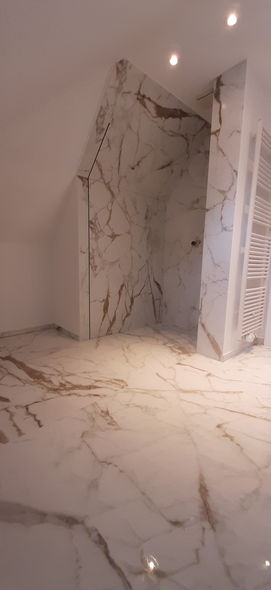 Wykończona łazienka z płytkami imitującymi marmur na podłodze i ścianach prysznica typu walk-in, widoczny grzejnik drabinkowy.