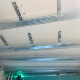 Markbud - Metalowy stelaż sufitu podwieszanego, przymocowany do sufitu za pomocą wieszaków, widoczny laser poziomujący, przygotowanie do montażu płyt gipsowo-kartonowych.