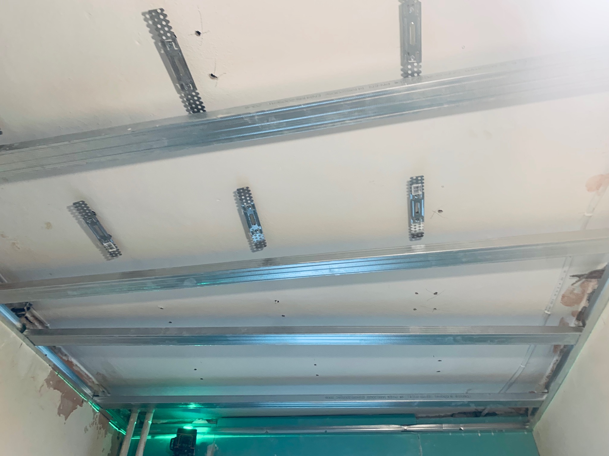 Metalowy stelaż sufitu podwieszanego, przymocowany do sufitu za pomocą wieszaków, widoczny laser poziomujący, przygotowanie do montażu płyt gipsowo-kartonowych.