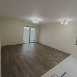 Fragment pokoju z częściowo ułożonymi panelami podłogowymi w odcieniach brązu, widoczne narzędzie do układania paneli i przygotowane podłoże pod dalszą część podłogi.