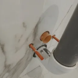 Montaż instalacji wodno-kanalizacyjnej w łazience z marmurowymi płytkami, widoczne rury PCV i peszle w ścianie.