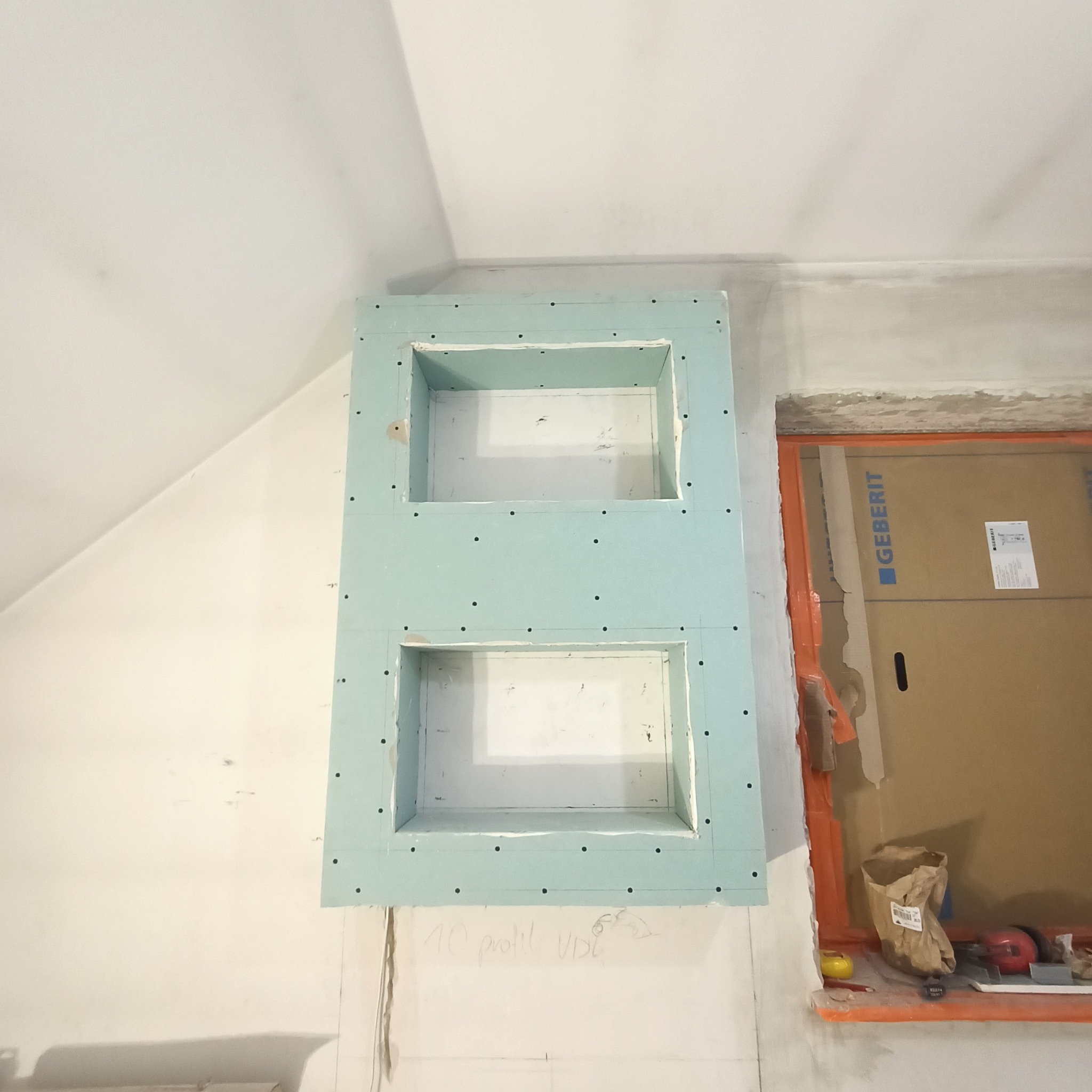 Dwie wnęki z płyty karton gips, przygotowane do wykończenia, na ścianie w trakcie prac remontowych. Widoczny kartonowy karton Geberit i narzędzia.