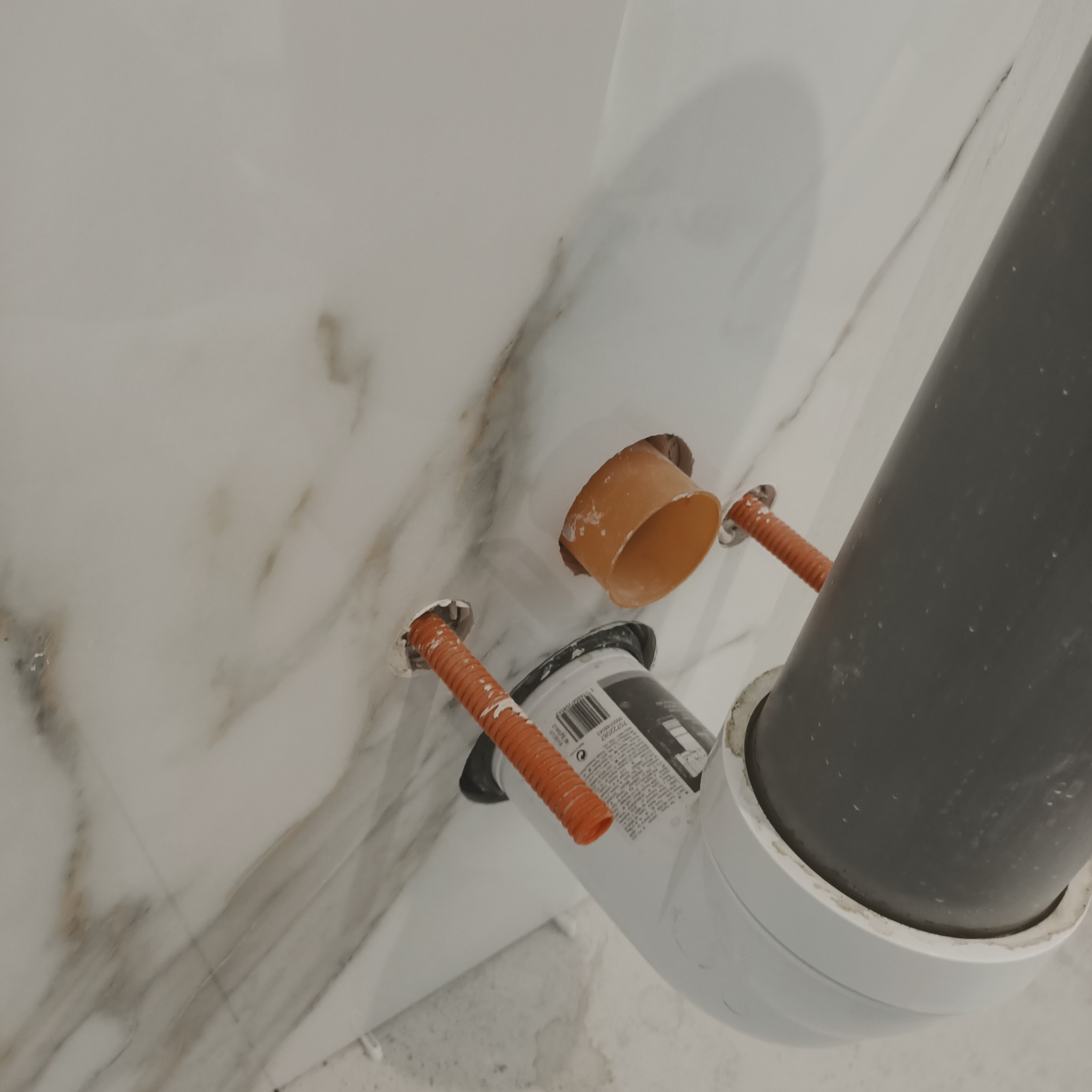 Montaż instalacji wodno-kanalizacyjnej w łazience z marmurowymi płytkami, widoczne rury PCV i peszle w ścianie.