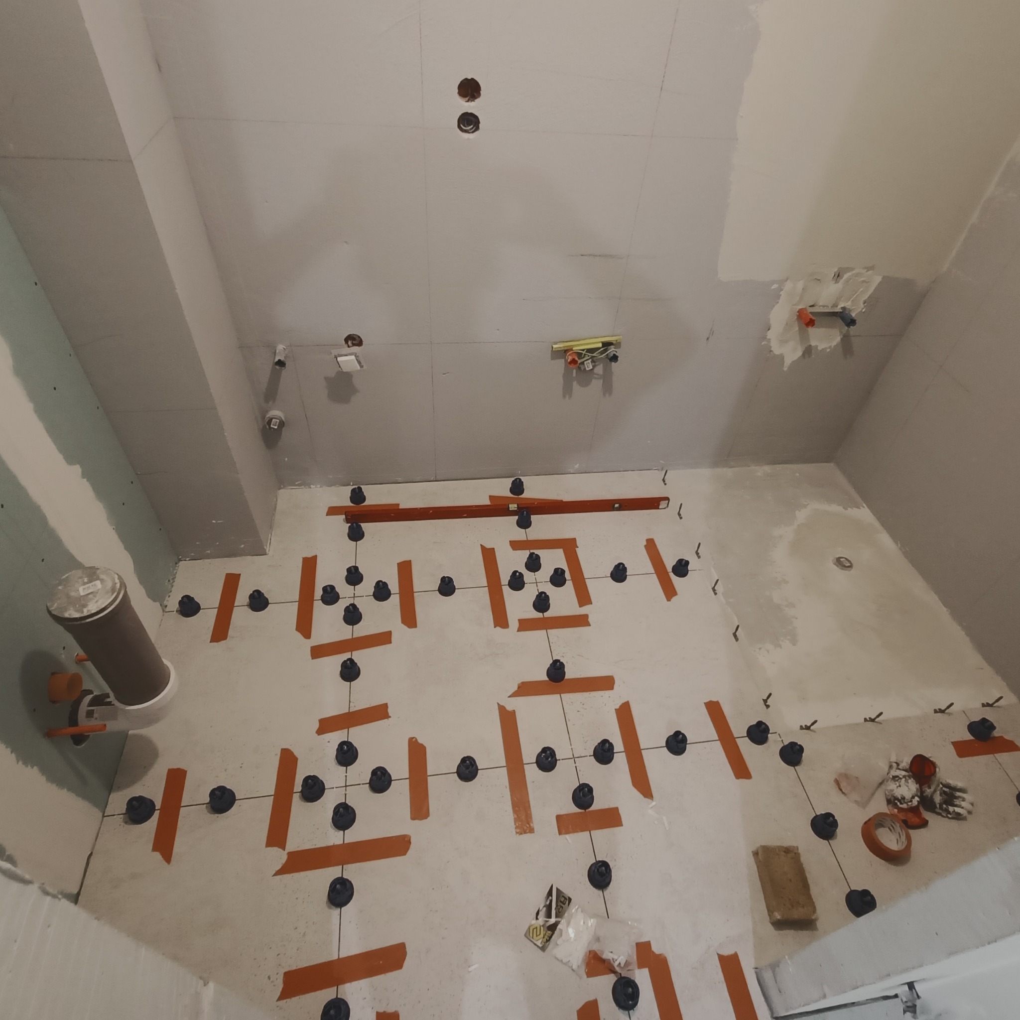 Układanie płytek podłogowych w łazience w Kutnie, z użyciem systemu poziomowania płytek (klipsy i kliny) oraz taśmy maskującej, widoczne przygotowane ściany i instalacje.