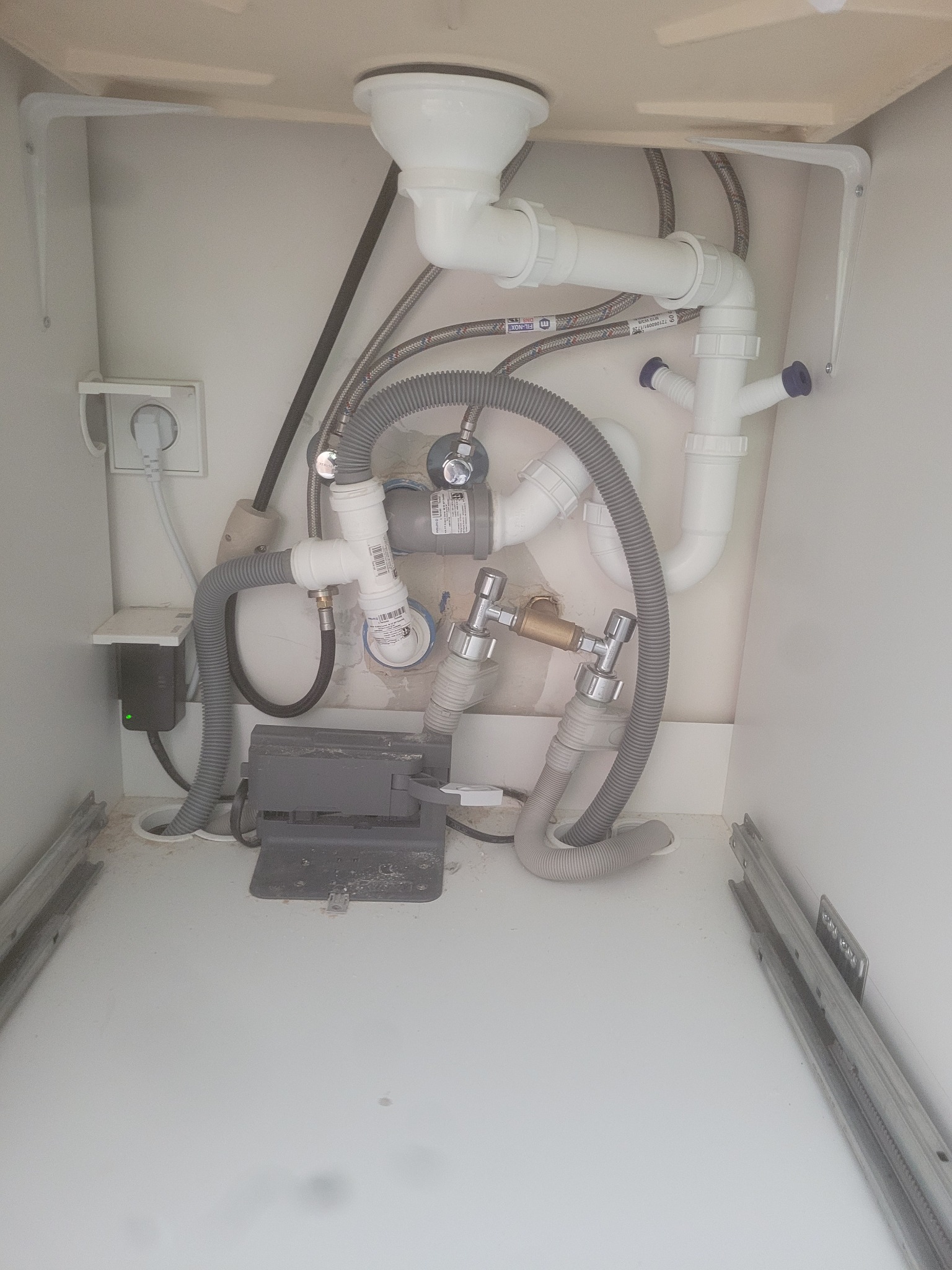 Złożona instalacja hydrauliczna pod zlewem w szafce, widoczne rury, zawory i węże. Prace hydrauliczne w Bydgoszczy.