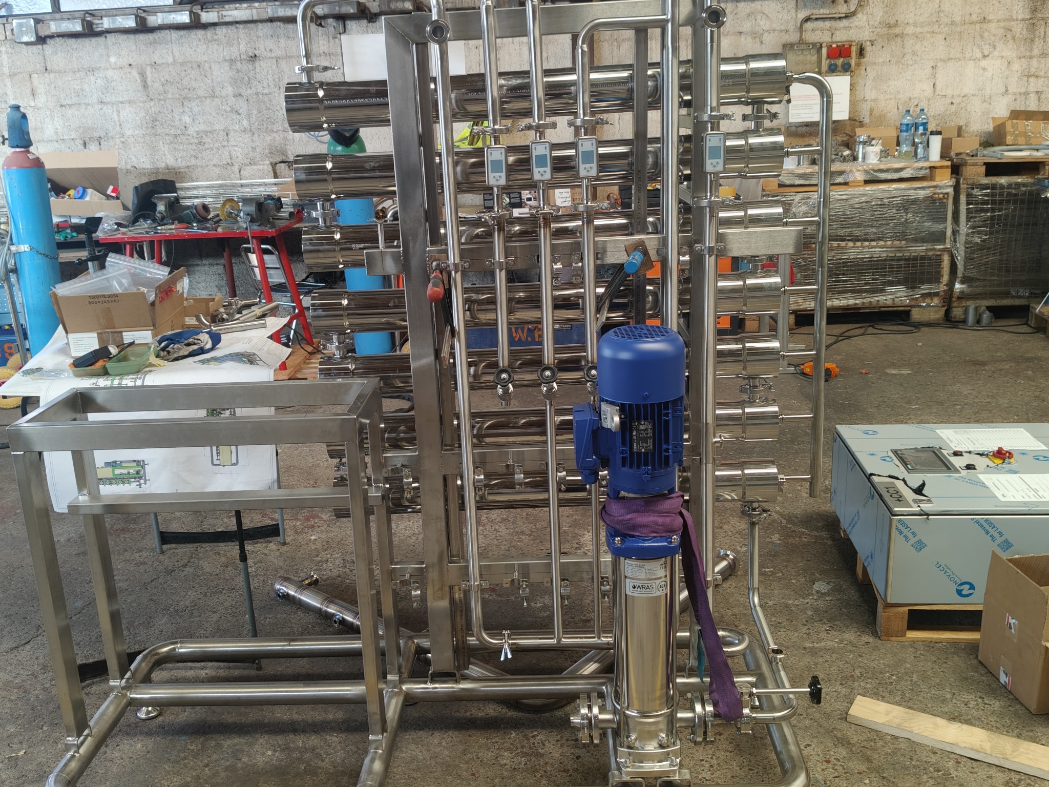 Kompleksowa konstrukcja ze stali nierdzewnej z niebieskim silnikiem i manometrami, w tle warsztat z narzędziami i materiałami. Precyzyjne wykonanie, detale.