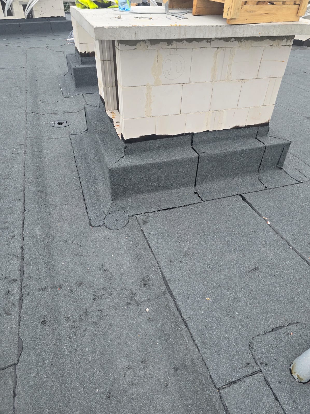 Szczegółowe ujęcie dachu pokrytego papą, z obróbką komina wykonaną z bloczków i zabezpieczoną papą. Widoczne detale łączeń i wykończeń.