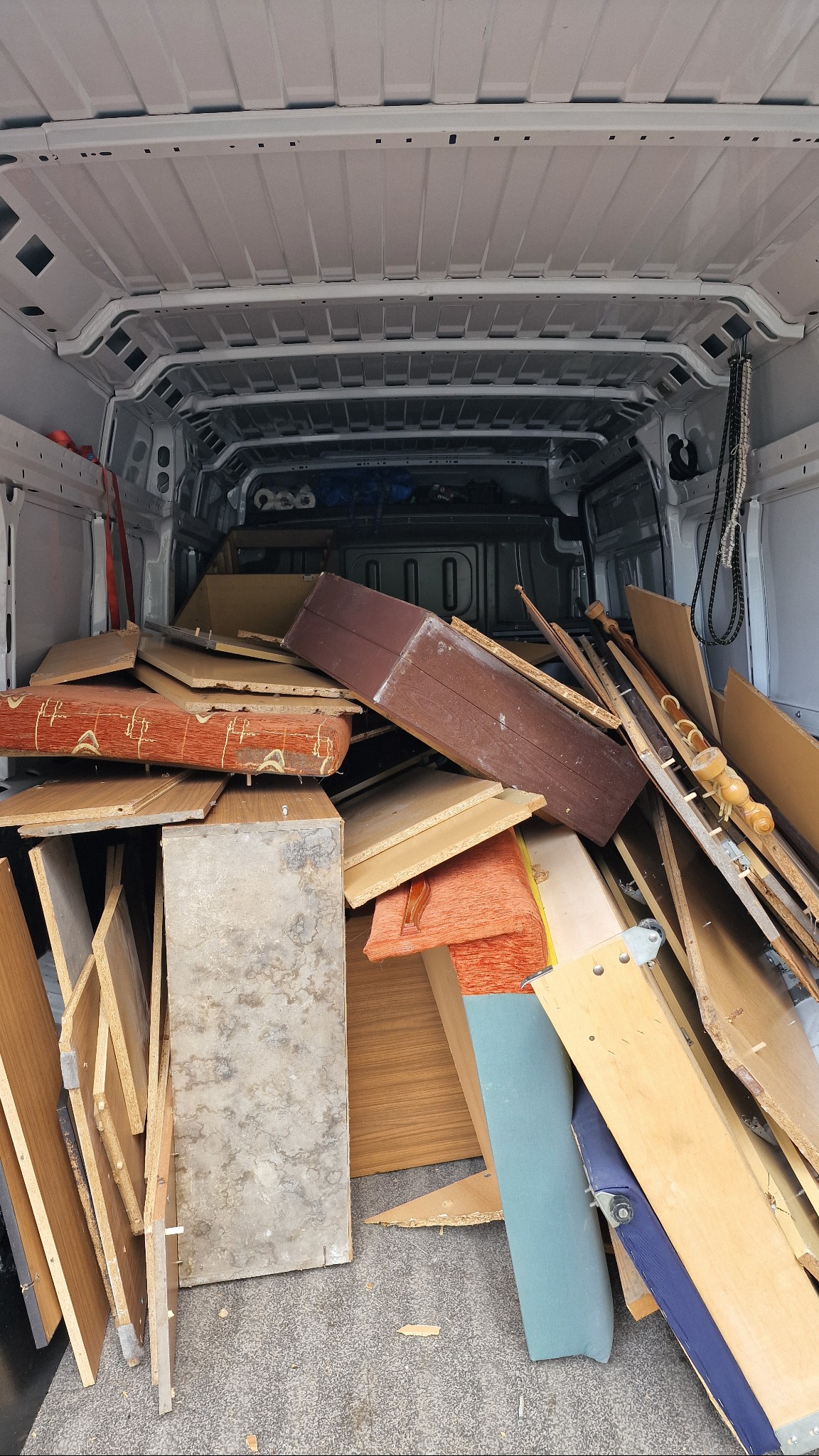 Wnętrze białego furgonetki wypełnionej elementami mebli i drewnianymi odpadami, przygotowanymi do transportu lub utylizacji.