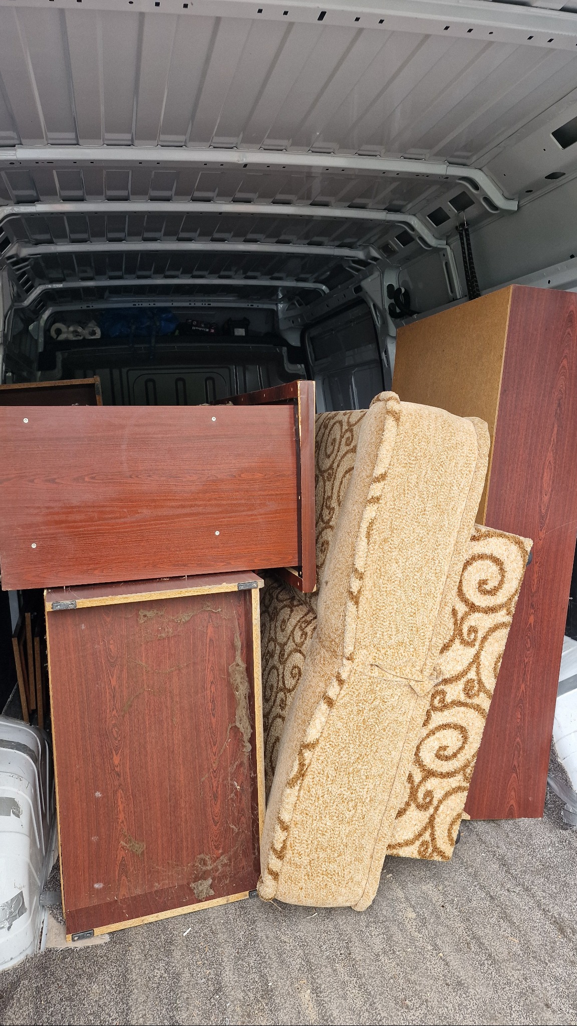 Wnętrze furgonetki załadowane meblami: drewniane szafki i beżowa sofa z wzorem, gotowe do transportu. Widoczne ślady użytkowania na meblach.