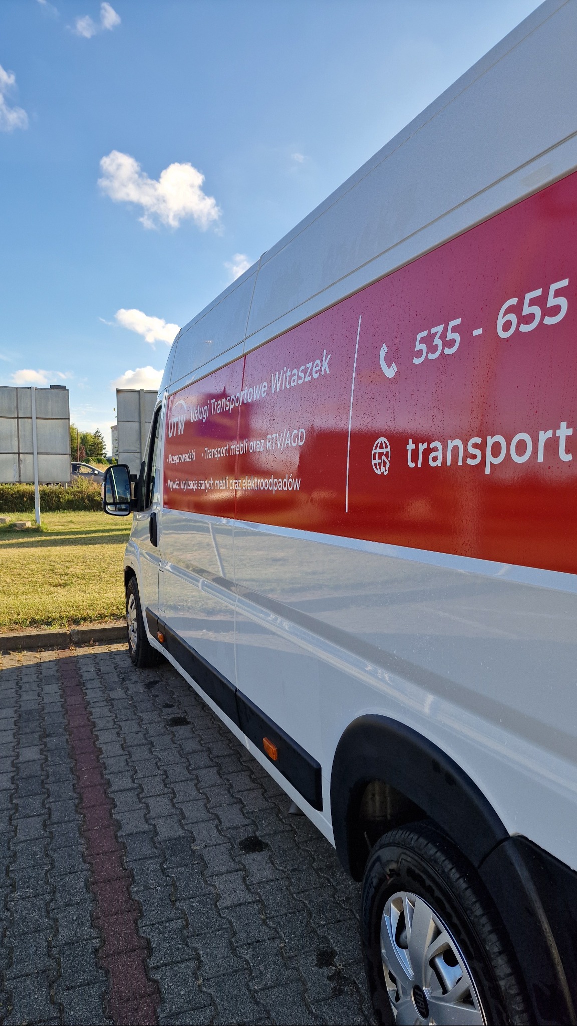 Biały bus z czerwonym logo firmy transportowej UTW na parkingu. Widoczne dane kontaktowe i zakres usług: przeprowadzki, transport mebli, utylizacja.
