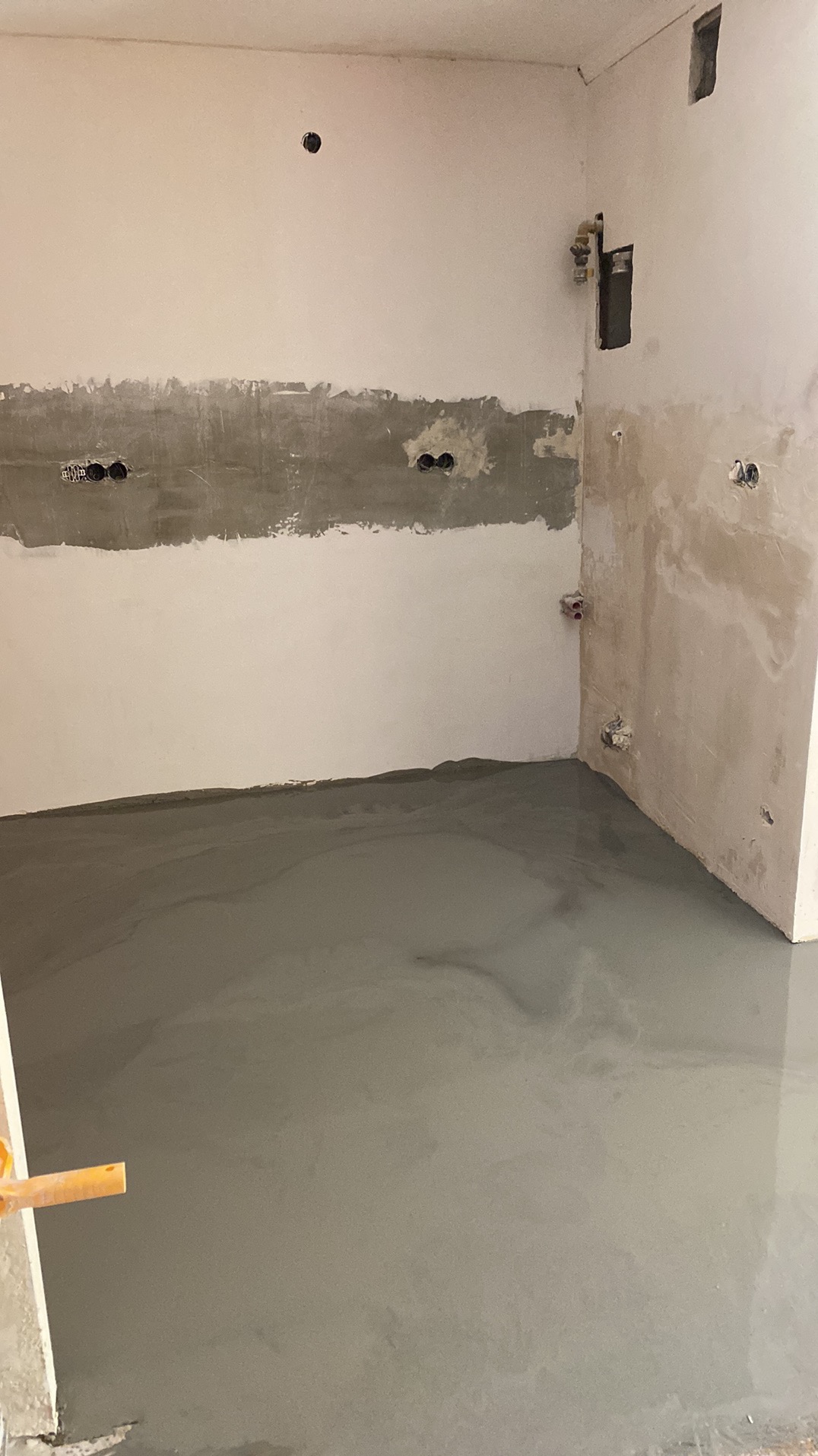 Świeżo wylany, mokry podkład podłogowy w pomieszczeniu z przygotowanymi ścianami, widoczne puszki elektryczne i wyprowadzenia wodne.