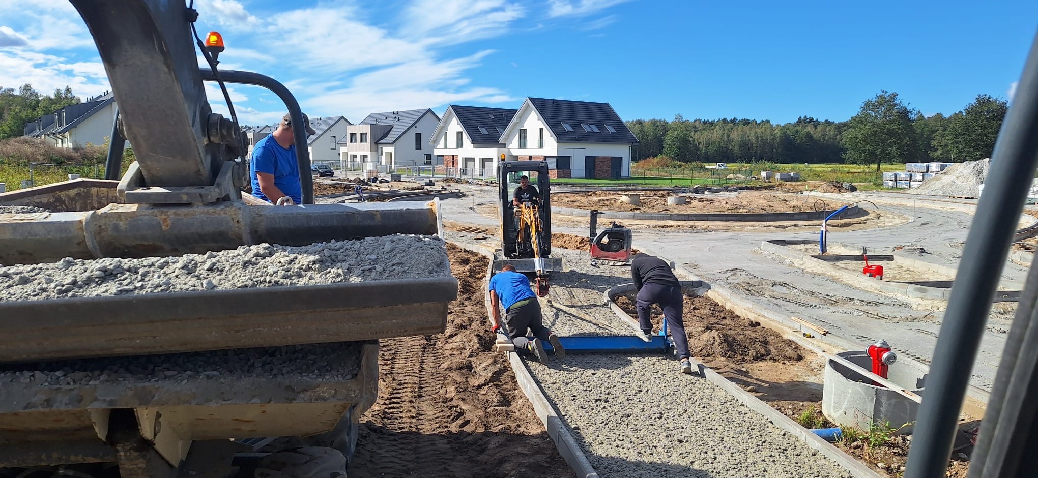 Ekipa budowlana w trakcie wyrównywania podłoża pod chodnik na osiedlu domów jednorodzinnych, z użyciem minikoparki i specjalistycznych narzędzi do niwelacji.