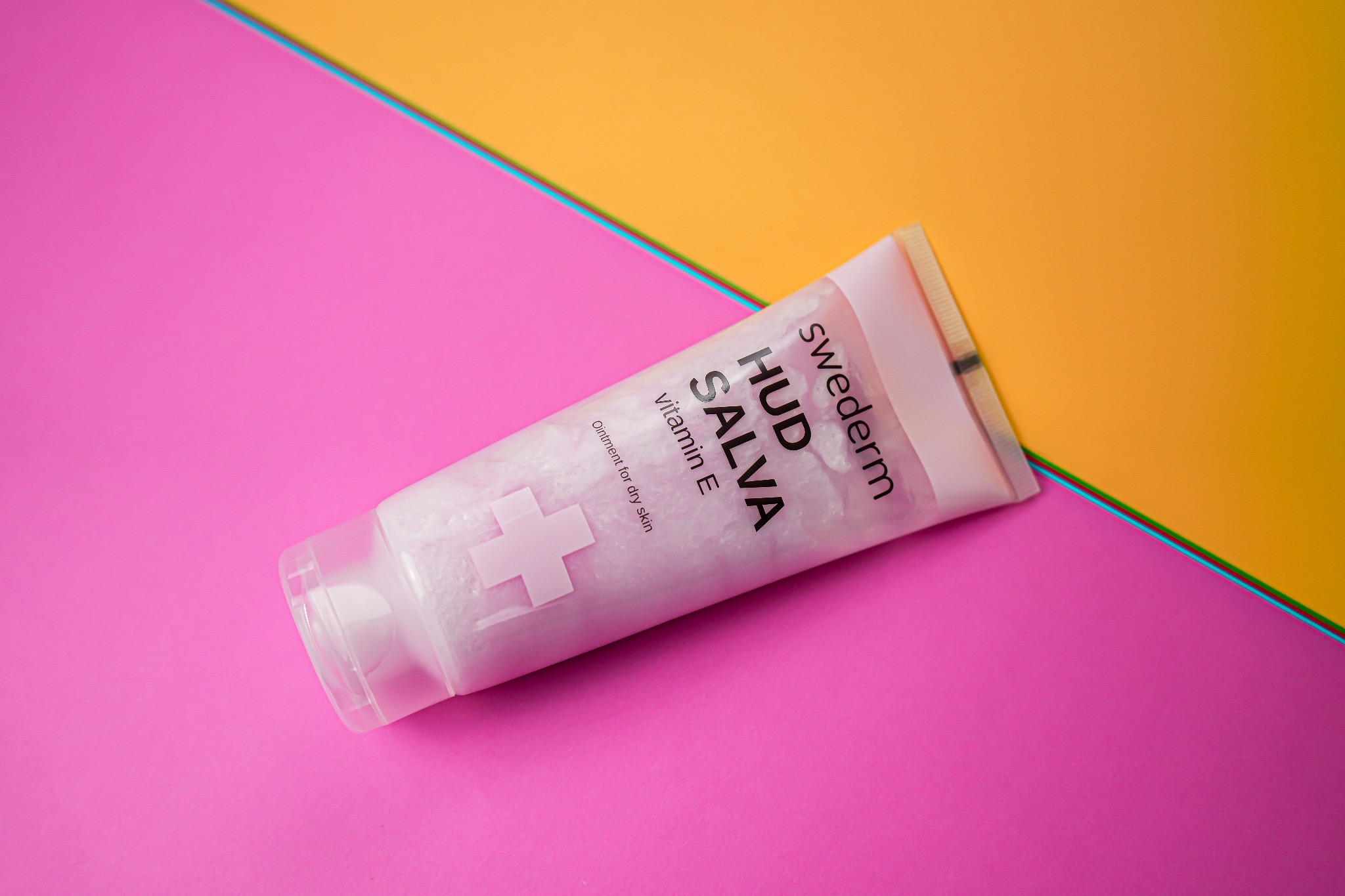 Różowa tuba kremu Swederm Hud Salva z witaminą E na tle w kolorach różowym, żółtym i turkusowym.