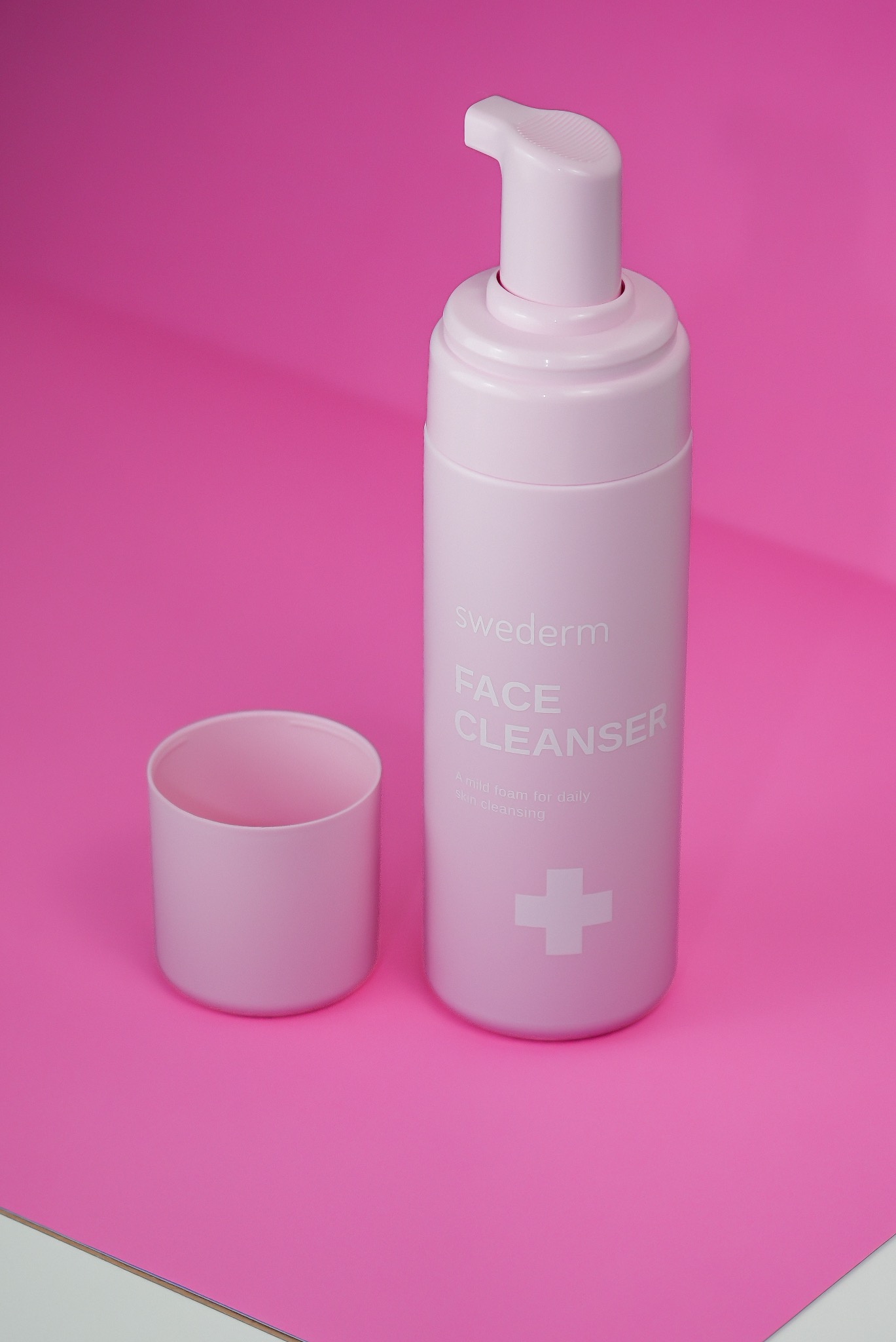 Różowa butelka z pompką i otwartym wieczkiem kosmetyku do mycia twarzy Swederm na różowym tle z delikatnym cieniem.