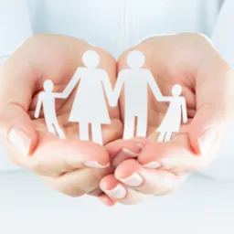 Dłonie kobiece trzymają wycięte z białego papieru postacie rodziny na białym tle.