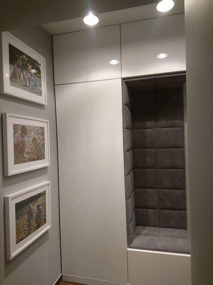 Biała szafa wnękowa z wbudowanym, tapicerowanym siedziskiem w kolorze szarym, udekorowana trzema ramkami ze zdjęciami na ścianie.