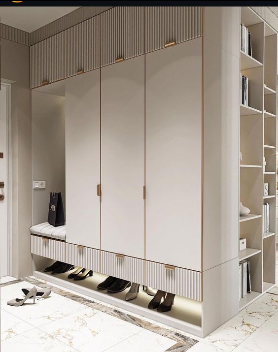 Biała szafa wnękowa z siedziskiem i półkami na buty, oświetlenie LED u dołu, marmurowa podłoga, torba zakupowa na siedzisku, minimalistyczne uchwyty.