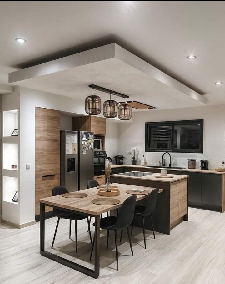 Nowoczesna kuchnia z wyspą i drewnianymi akcentami, oświetlenie punktowe i dekoracyjne lampy wiszące nad stołem jadalnym, minimalistyczny design z czarnymi krzesłami.