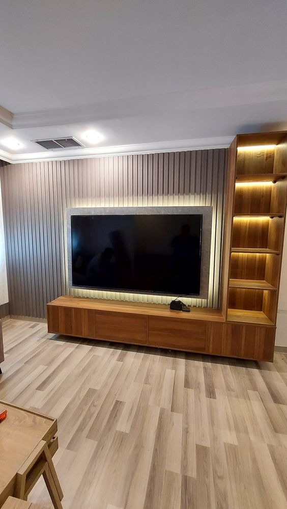 Nowoczesna ściana telewizyjna z drewnianymi panelami, podświetleniem LED i regałem z oświetleniem wewnętrznym, na tle parkietu.