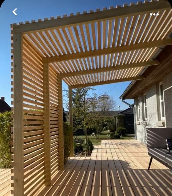 Drewniana pergola z listew na tarasie, tworząca zacienione miejsce do wypoczynku, z widokiem na zadbany ogród.