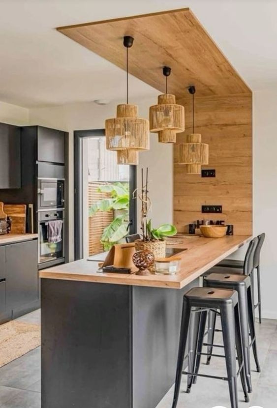 Nowoczesna kuchnia z wyspą i drewnianymi akcentami, oświetlona trzema lampami z naturalnego sznurka, z widokiem na zieleń za oknem.