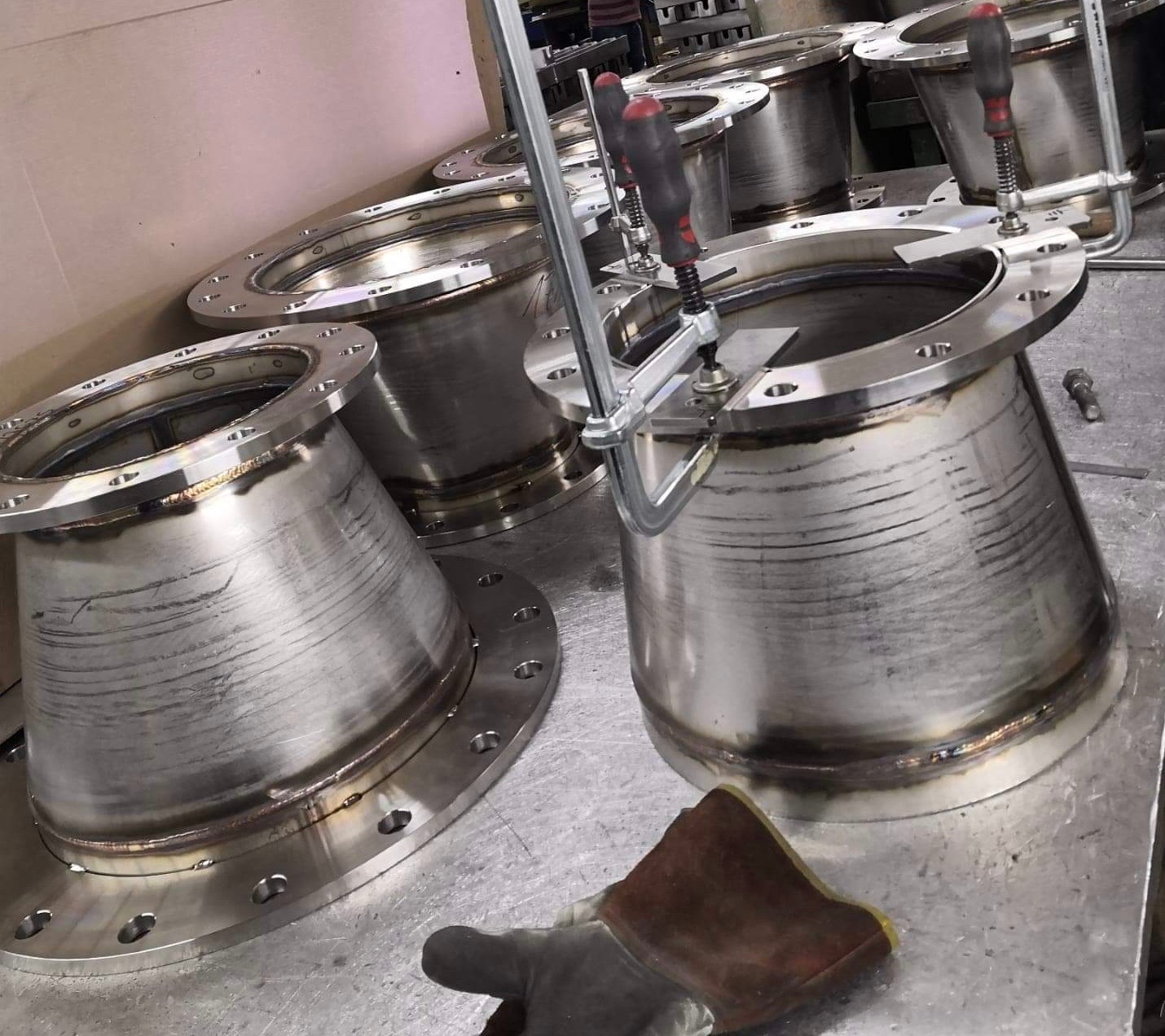 Konstrukcje stożkowe ze stali nierdzewnej z kołnierzami, z widocznymi śladami obróbki i spawania, zabezpieczone zaciskami śrubowymi podczas procesu łączenia.