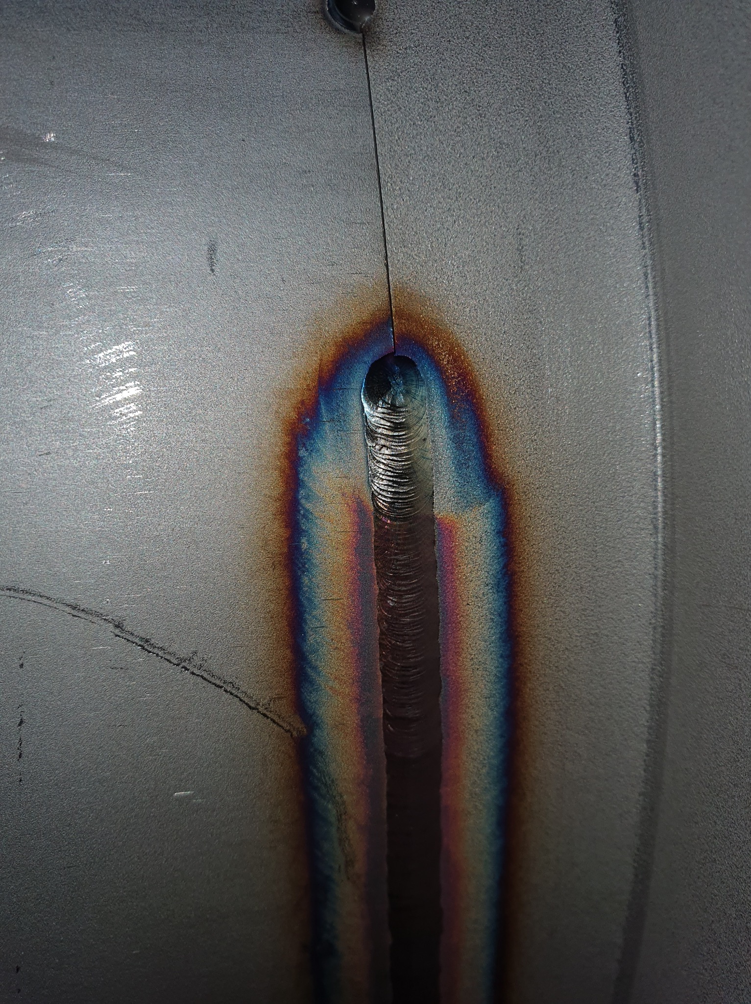 Zbliżenie na spoinę na metalowej powierzchni, widoczne tęczowe zabarwienie wokół spoiny, ukazujące precyzję wykonania.