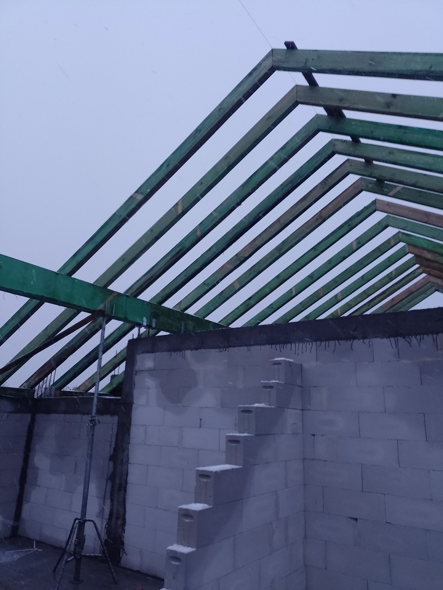 Surowe ściany z betonu komórkowego z widoczną konstrukcją drewnianą dachu w trakcie budowy, podpartą metalowym stemplem.